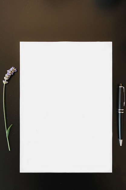 Photo vertical white sheet of paper next to a lavender and a pen lie on a dark table