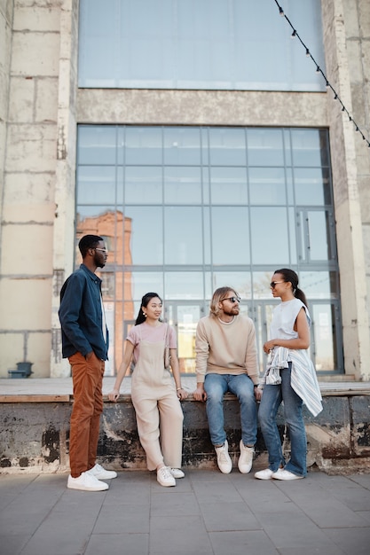 Vertical wide angle view at diverse group of contemporary young\
people chatting outdoors in urban city setting