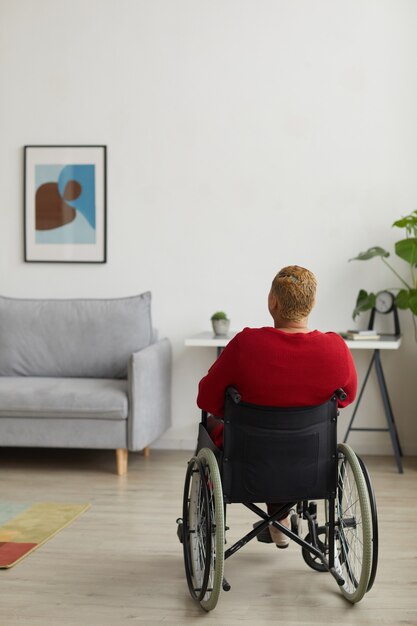 Verticale achteraanzicht bij moderne vrouw met een handicap die rolstoel gebruikt in een minimaal interieur, kopieer ruimte