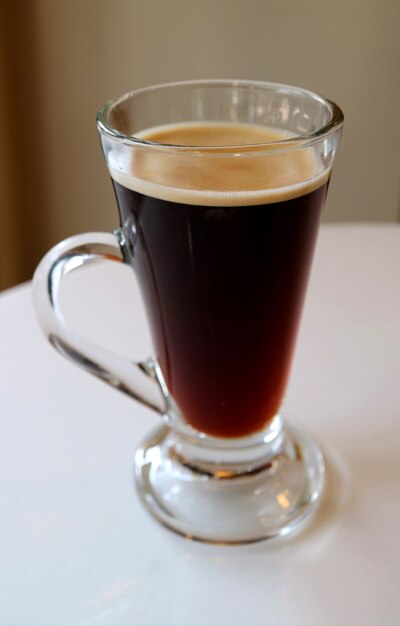 Verticale afbeelding van hete zwarte koffie in transparant glas geïsoleerd op witte tafel