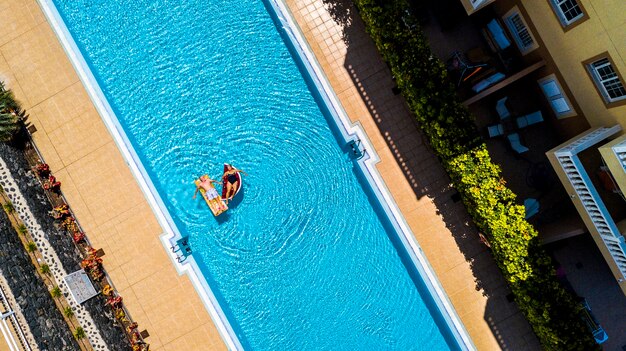 Verticale bovenaanzicht van zwembad in hotelresidentie vakantie met mensen volwassen senior liggen en genieten met springkussens lilos matras op blauw water