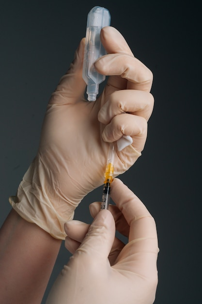 Verticale close-up studio-opname van onherkenbare arts in witte handschoenen die vaccin vasthoudt en opvult...