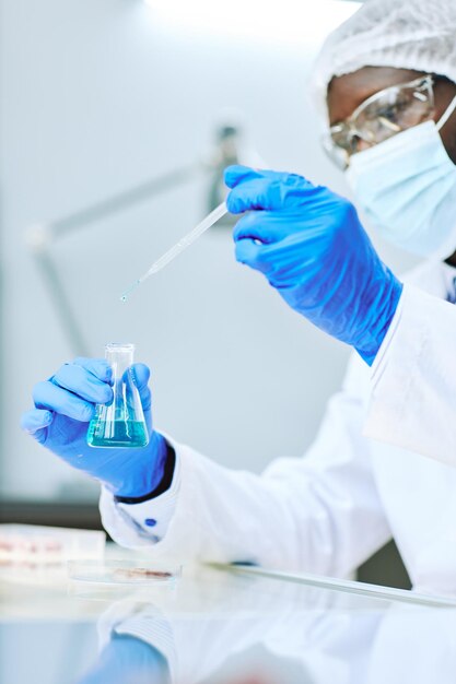 Verticale close-up van Afro-Amerikaanse laboratoriumtechnicus die vloeibare monsters neemt met een pipet