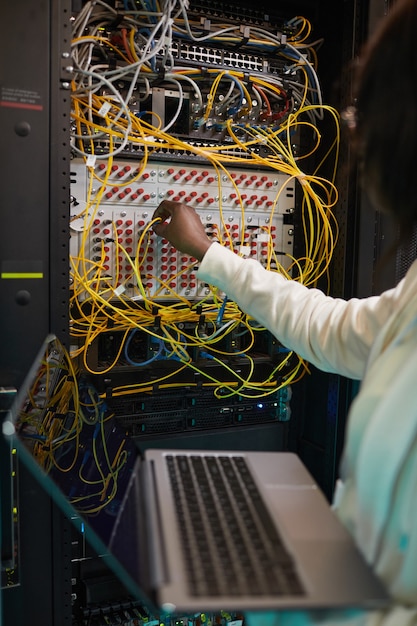 Verticale close-up van vrouwelijke netwerkingenieurs die kabels aansluiten in serverkast tijdens het werken met supercomputer in datacenter, kopieer ruimte