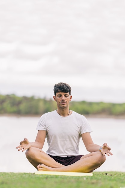 Verticale foto van een atletische man met sportkleding die de lotuspositie van yoga in een park doet