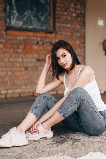 Verticale foto van een brunette vrouw in spijkerbroek zit op de grond Het meisje maakt haar haar recht