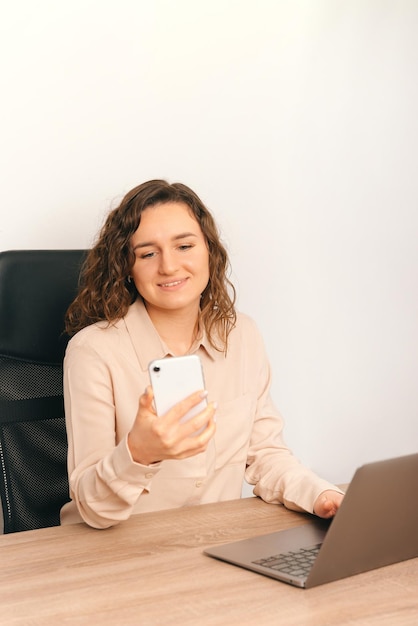 Verticale foto van een charmante jonge vrouw die op kantoor op kantoor zit en smartphone gebruikt