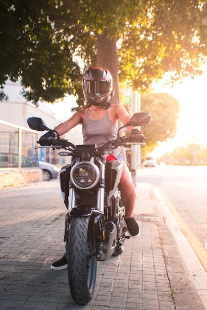 Verticale foto van een fietservrouw klaar om met haar motorfiets uit te gaan. De mooie zon wijst op fotografie van frontale motor.