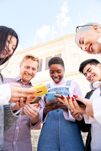 Foto verticale foto van een groep multiraciale vrienden die samen buiten plezier maken met behulp van een mobiele telefoon