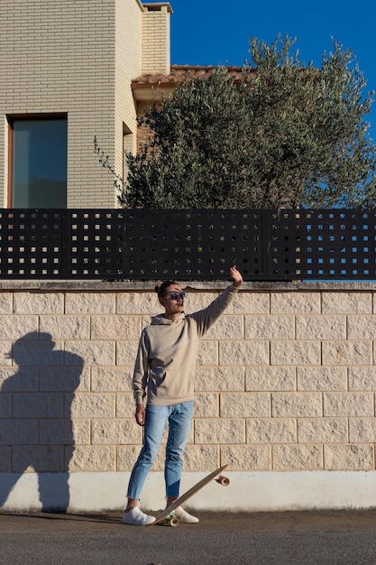 Verticale foto van een jonge skater-tiener die zich voor de zon verstopt met zijn hand die schaduwen op zijn gezicht creëert