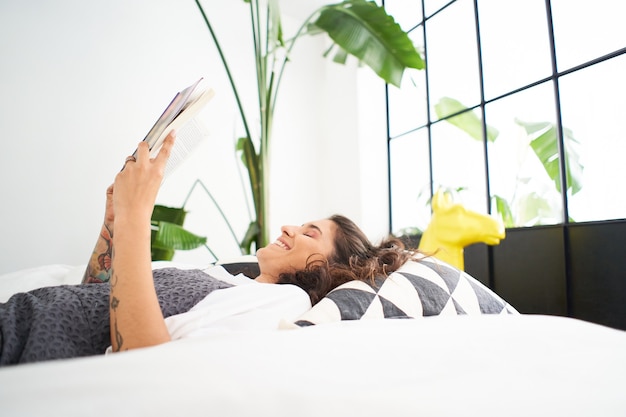 verticale foto van een jonge vrouw die een boek leest in de gezellige kamer die de pagina omslaat en leert studeren