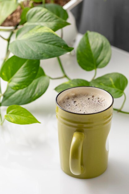 Verticale foto van een kopje koffie naast wat planten en wat boeken op de achtergrond met ruimte voor tekst