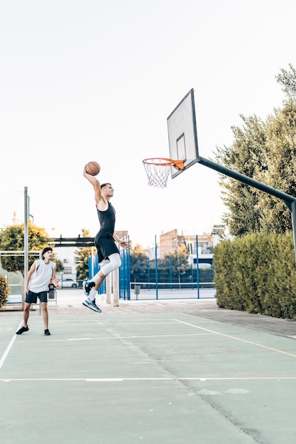 Verticale foto van een lange man die springt terwijl hij scoort tijdens een vriendschappelijke basketbalwedstrijd buiten