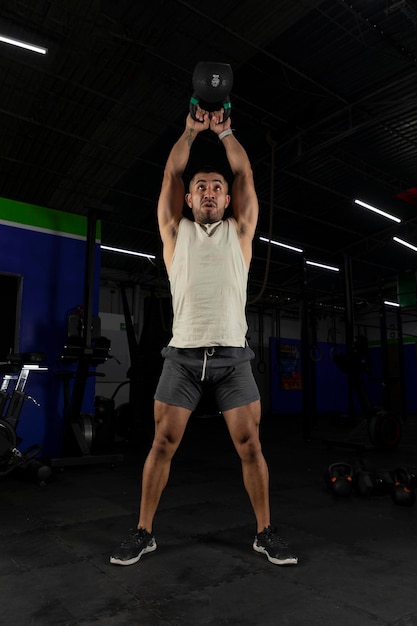 Verticale foto van een latijnse man die traint met een kettlebell in een sportschool die rechtop staat