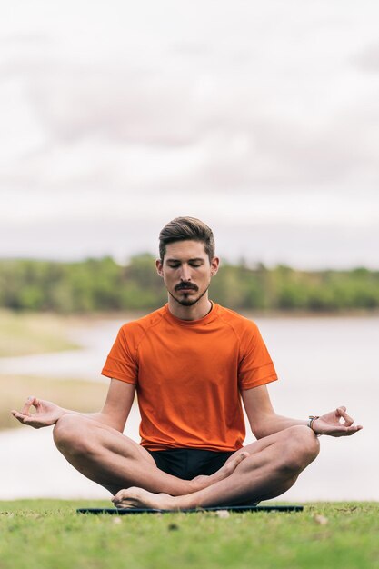 Verticale foto van een man met een regenboogarmband die de lotushouding van yoga in een park doet