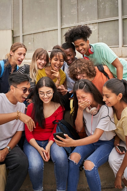 Verticale foto van een multi-etnische groep studenten die een mobiele telefoon gebruiken en lachende tieners die een...