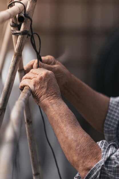 Verticale foto van een oude man die buitenshuis een rietconstructie maakt