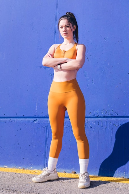 verticale foto van een serieuze sportvrouw poseren met gekruiste armen kijkend naar de camera voor een blauw muurconcept van sport en actieve levensstijl