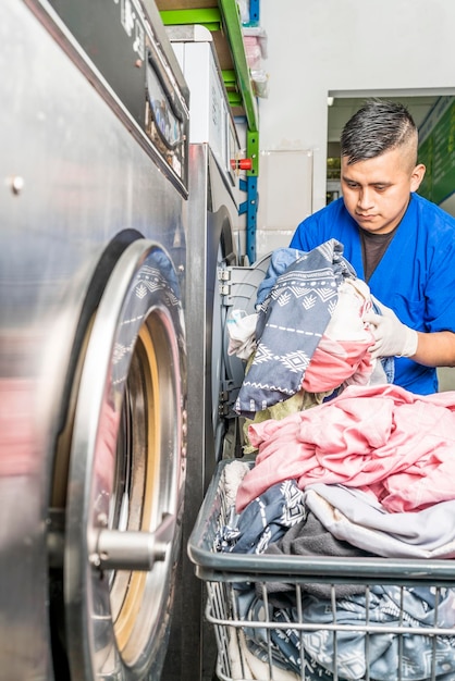 Verticale foto van een werknemer die kleding in een industriële wasmachine steekt