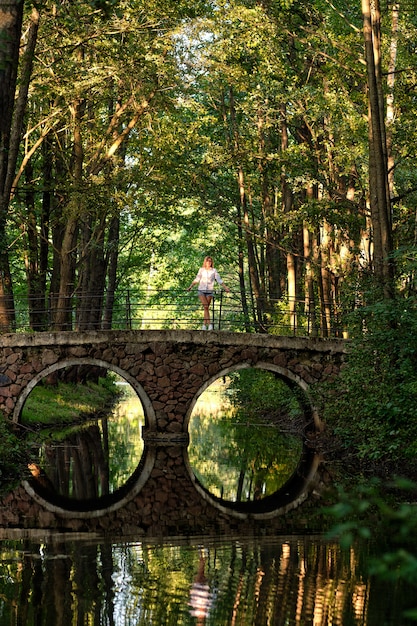 Verticale foto van lange afstand van meisje op stenen brug over kleine rivier in park