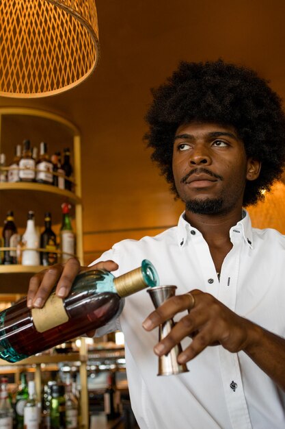Verticale foto van Latijnse barman die met krullend haar een cocktail klaarmaakt