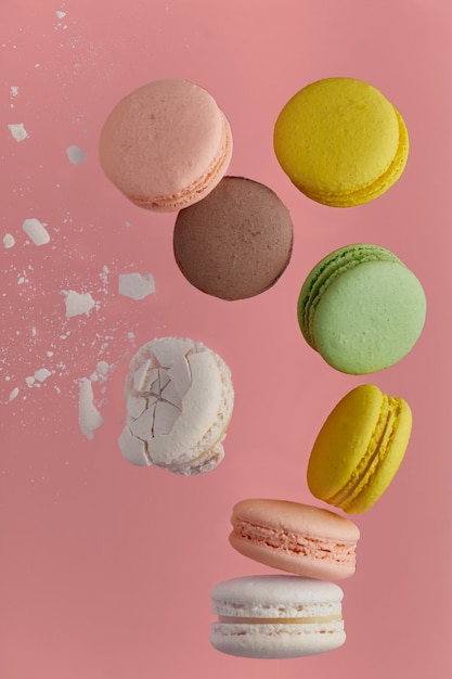 Verticale foto van makaron. kleurrijke cake macaron met pasteltinten en witte gebarsten macaron met kruimels in chaotische levitatie vallen op de stapel op roze muur. bovenaanzicht van amandelkoekjes.