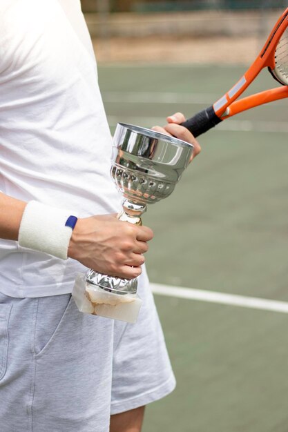 Foto verticale foto van onherkenbare professionele tennisspeler met een beker en een racket in zijn handen.