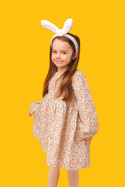 Verticale foto van schattig een klein meisje met paasoren en een prachtige jurk Studio-opname over gele achtergrond