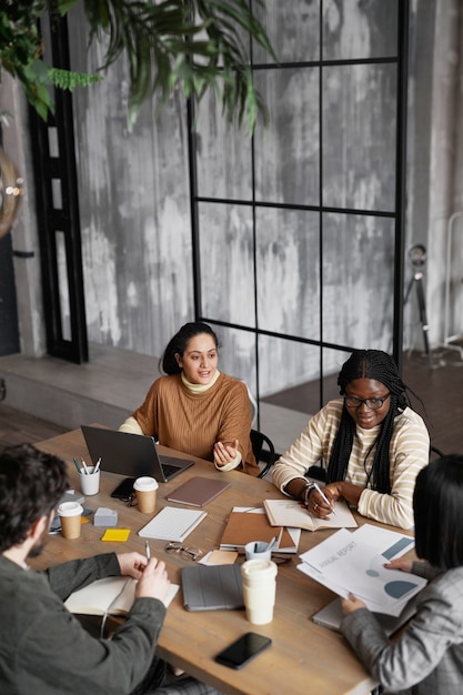 Verticale hoge hoekmening bij diverse groep zakenmensen die bijeenkomen aan tafel in een elegant kantoorinterieur, kopieer ruimte