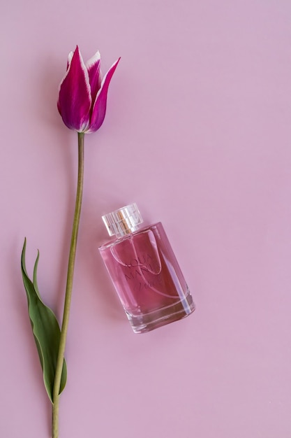 Verticale lila achtergrond met een prachtige lentetulp en een kristallen fles parfum of tualct water bovenaanzicht een kopie van de ruimte