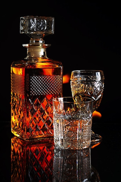 Verticale opname van een fles whisky en glazen met vlammen op een zwarte achtergrond