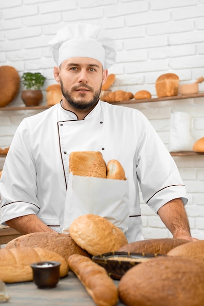 Verticale opname van een jonge, knappe bakker die in zijn bakkerij staat achter het display vol met verschillende heerlijke broden die koken koken voedsel chef-kok voeding verkopen retail zakenman boodschappen.