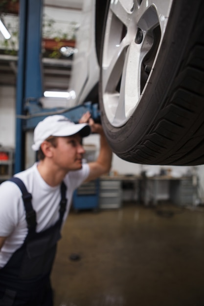 Verticale opname van een monteur die onder een auto op een autolift kijkt