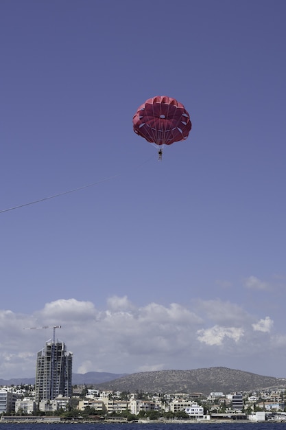 Verticale opname van een parachutespringende man in een heldere blauwe lucht die over de stad vliegt