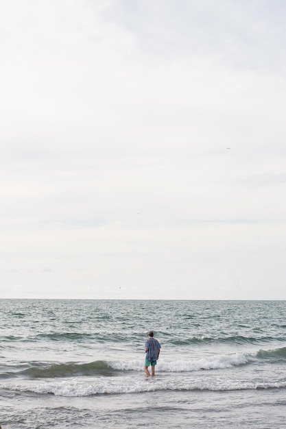 Verticale opname van een persoon alleen op het strand op een bewolkte hemelachtergrond