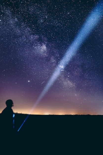 Foto verticale opname van een persoon die de zaklamp naar de hemel richt met de melkweg