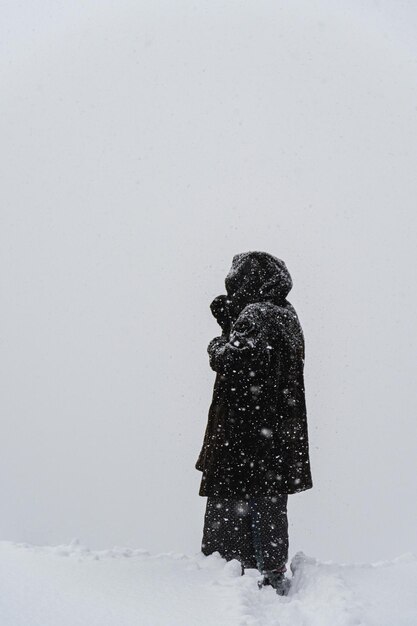 Verticale opname van een vrouw met een warme harige winterjas die buiten staat tijdens zware sneeuwval