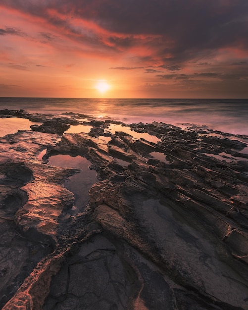 Verticale opname van het rotsachtige strand en de oceaan tijdens zonsopgang