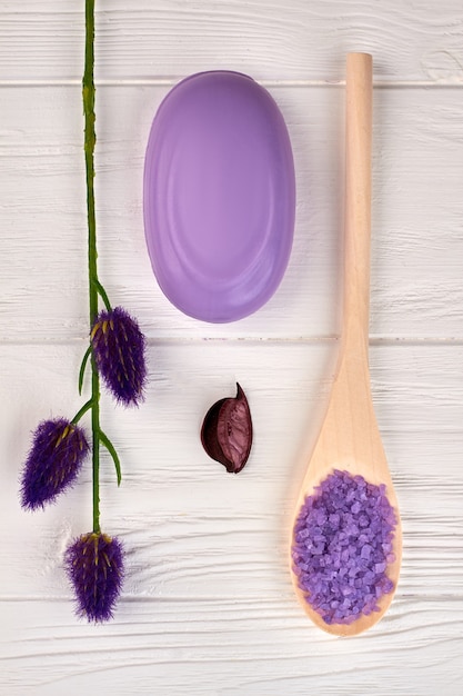 Verticale shot paarse accessoires voor spa-behandeling. Zeep met zout en lavendel. Witte houten achtergrond.