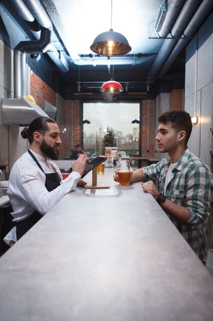 Foto verticale shot van een barman praten met mannelijke klant over de toonbank bij biercafé