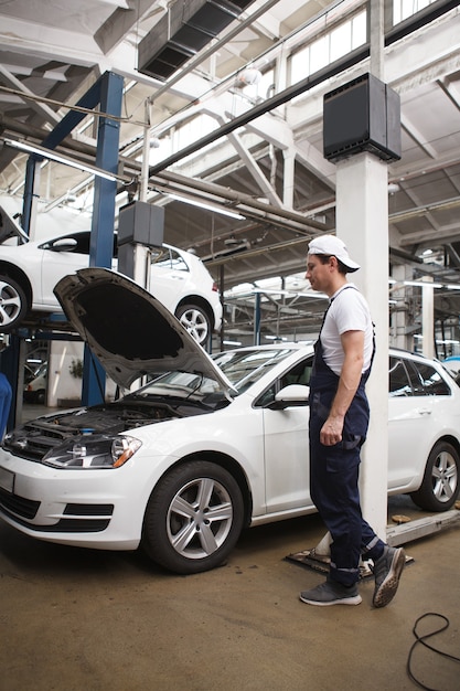 Verticale volledige lengte van een autoservicemedewerker die een kapot voertuig onderzoekt