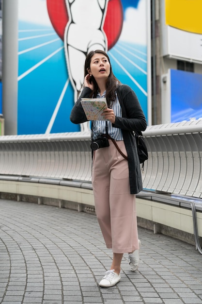 verticale volledige lengte van verwarde Aziatische meisjesreiziger die kaart vasthoudt en afstanden onderzoekt zonder idee welke kant op te gaan in Shinsaibashi Suji en Doutonbori Osaka Japan in de buurt van Glico Man Sign