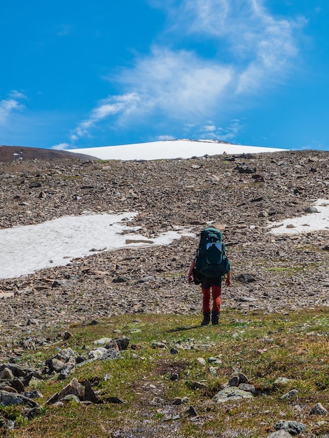 Verticale weergave solo trekking in de bergen. Man met een grote rugzak klimt zwaar op een bergpad. Avontuurlijk solo reizend lifestyle-concept, actieve weekendvakanties in de wilde natuur