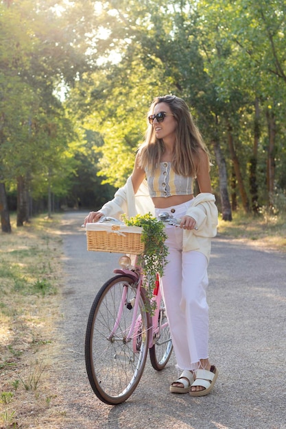 Verticale weergave van een jonge vrouw die naar de zijkant kijkt op een roze retrofiets omringd door de natuur