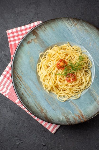 Verticale weergave van heerlijke spagetti geserveerd met tomatengroen op rode gestripte handdoek op zwarte achtergrond