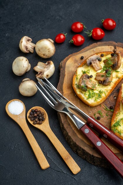 Verticale weergave van smakelijke snack met paddestoelenbestek op een houten bord en kruiden rauwe groenten op zwarte achtergrond