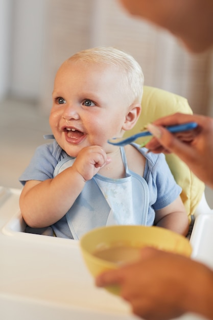 Verticall shot of unrecognizable woman feeding her cheerful baby son with porridge