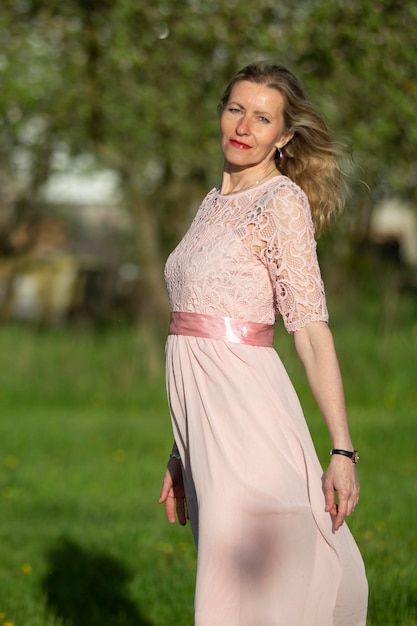 Vertically beautiful elderly woman in a pink dress on a background of green nature