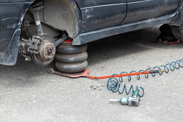 Vervangen van het wiel op het bandenservicecentrum. Vuile zwarte auto zonder een wiel opgetild op de pneumatische krik in een autoreparatiewerkplaats