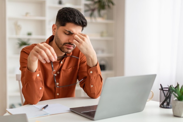 Verveeld Arabische mannelijke werknemer zit aan bureau met pc